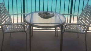 Un balcón con una mesa de vidrio y dos sillas, con vistas al mar turquesa y un cielo despejado.