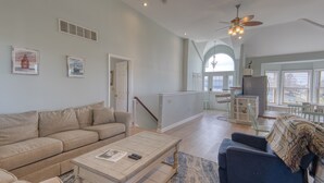 A spacious living room with a sofa, coffee table, and a blue armchair. There is a staircase leading to an upper level with a balcony. - Captain's Quarters (Frederica)