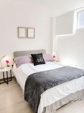 A bedroom with a bed, bedside tables, a window, and wall-mounted pictures.