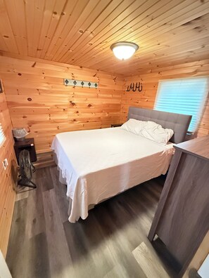 Une chambre dans une cabane en bois, avec un lit, une table de chevet et un petit radiateur.
