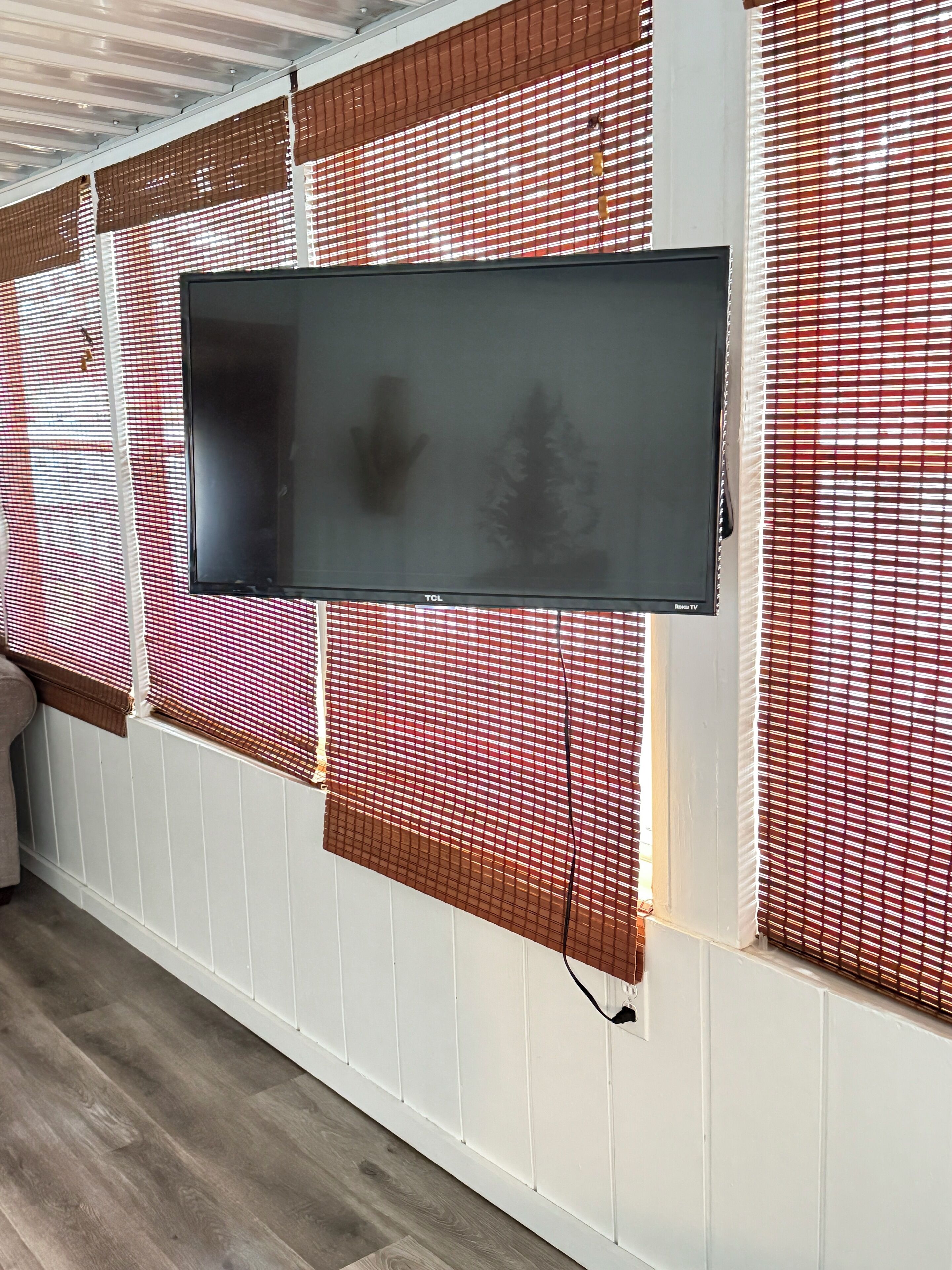 A flat-screen TV mounted on a wall with red and white blinds.