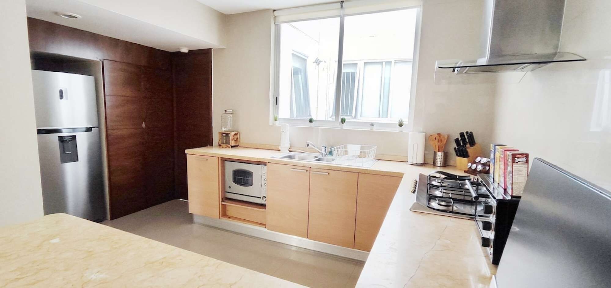 Cozinha moderna com forno embutido, geladeira de aço inoxidável e janela que traz luz natural.