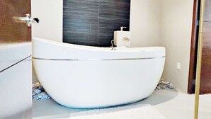Une salle de bain moderne avec une baignoire sur pieds, un mur foncé à texture marquée et un petit meuble blanc.