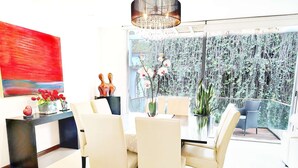 Un espace repas moderne avec une table en verre, des chaises blanches et une vue sur un balcon agrémenté de plantes.