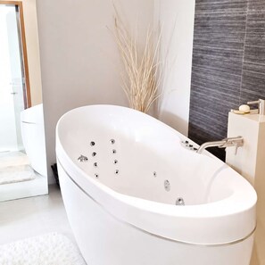 Een moderne badkamer met een vrijstaand bad, toilet en douche.