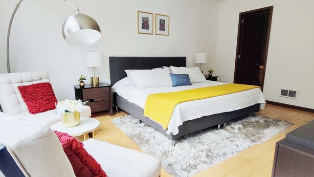 Une chambre à coucher moderne avec un lit, des tables de chevet, une chaise, une lampe et une porte.