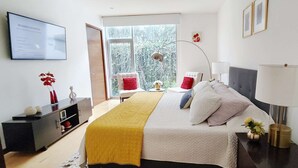 Une chambre à coucher moderne, avec un lit, des tables de chevet, un bureau et une fenêtre donnant sur des arbres.