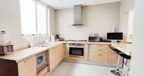 Een moderne keuken met een gasfornuis, oven en een magnetron. Er is een raam dat zorgt voor natuurlijk licht en een spoelbak met een afwasschaal.