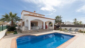 Une maison à deux étages avec une piscine, un patio couvert et un jardin agrémenté de palmiers.