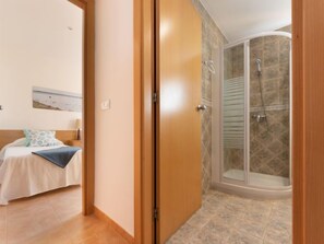 Une chambre d’hôtel avec un lit, une table de chevet, un tableau au mur et un espace douche doté d’une porte en verre.