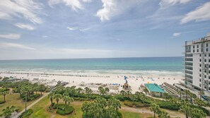 A beach view with a hotel in the foreground, a sandy beach, and a clear sky.