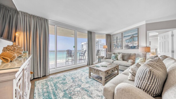 A spacious living room with a large sliding glass door leading to a balcony, a cozy sofa set, a coffee table, and a patterned rug.