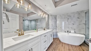 A modern bathroom with a freestanding bathtub, two sinks with gold faucets, and a large mirror above the vanity. - St. Maarten 907| Beachfront | Luxury 3BR (Destin)