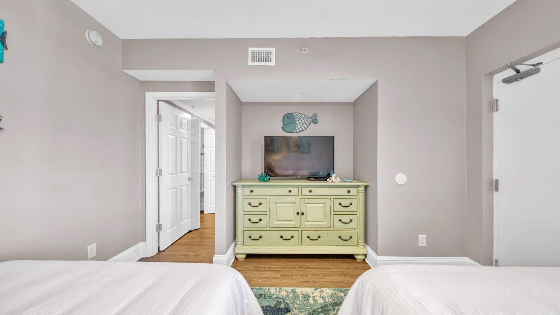 Une chambre avec deux lits, une commode verte, un objet de décoration représentant un poisson et un téléviseur.