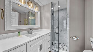 A modern bathroom with a large mirror, two sinks, a shower with glass doors, and a toilet.