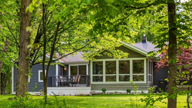 Ein Haus mit überdachter Veranda, Rasen und Bäumen.