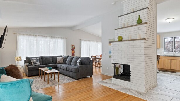 A modern living room with a grey sectional sofa, a teal armchair, and a white brick fireplace. - Bright "Mid-Century Modern" Ranch (Rochester)