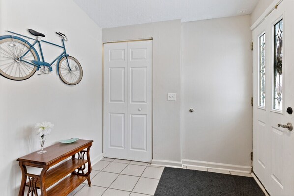 A hallway with a white door, a bicycle mounted on the wall, a wooden bench, and a small table with a vase of flowers. - Bright "Mid-Century Modern" Ranch (Rochester)