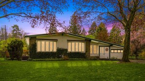 A single-story house with a garage, surrounded by a well-maintained lawn and trees. - Bright "Mid-Century Modern" Ranch (Rochester)