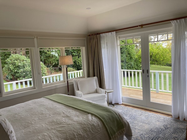 A bedroom with a large bed, a chair, a lamp, and a view of a balcony with greenery.