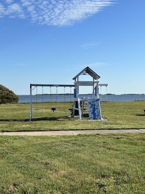A playground with swings and a covered seating area near a body of water.