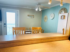 A dining area with wooden chairs and a table, a ceiling fan, and wall decorations.
