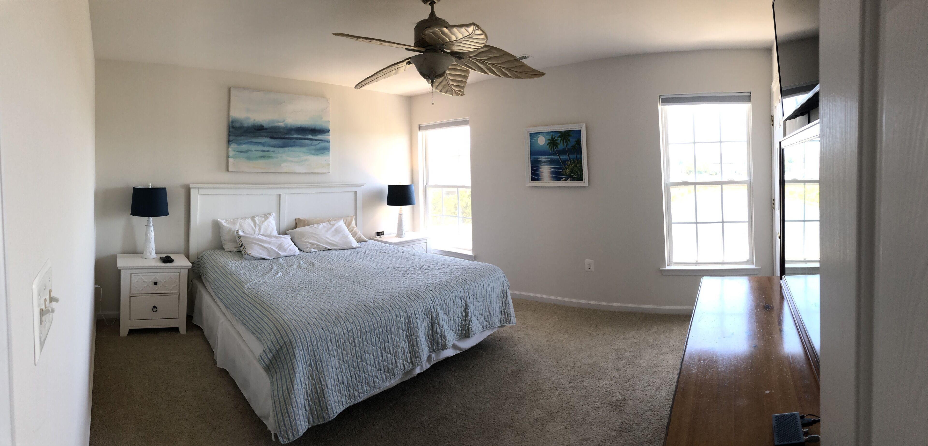 A bedroom with a bed, nightstands, a ceiling fan, and two windows.