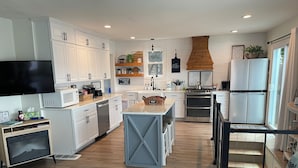 Una cucina moderna con mobili bianchi, un'isola centrale, elettrodomestici in acciaio inossidabile e un soffitto in legno.