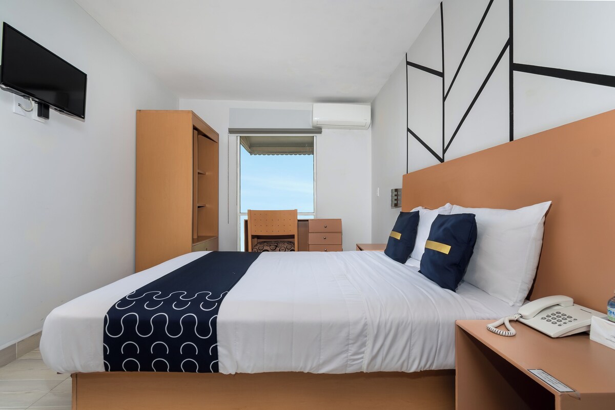 A hotel room with a bed, bedside table with a phone, and a view of the sky through an open door.