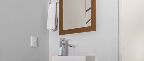 A bathroom with a white sink, wooden vanity, a mirror, and a towel hanging on the wall.
