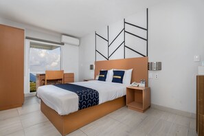 A modern hotel room with a large bed, a desk, and a view of the mountains through the window. - Hotel Plaza Regina Torreón (Torreón)