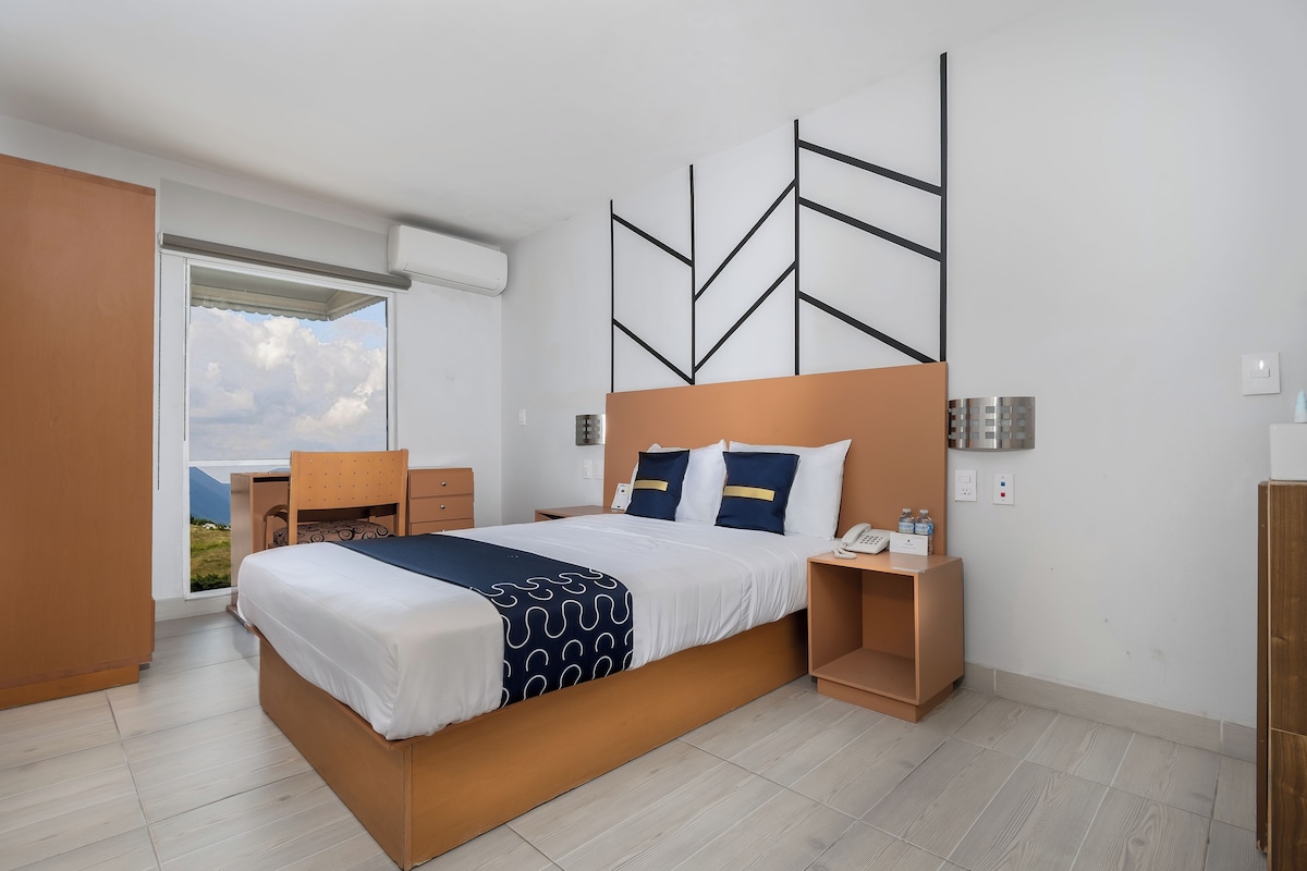 A modern hotel room with a large bed, a desk, and a view of the mountains through the window.