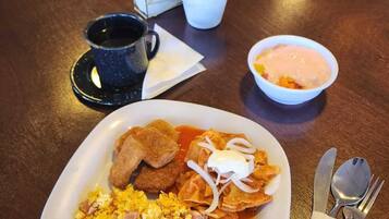 Un plato de huevos revueltos, frijoles refritos y papas picadas, acompañado de salsa y crema agria.