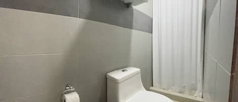 A bathroom with a toilet, a trash bin, a towel rack with a towel, and a shower curtain.