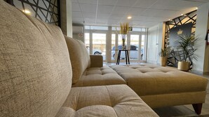 Un rebedor d'hotel modern amb un sofà beix gran, una taula petita amb un ram i una planta en test.