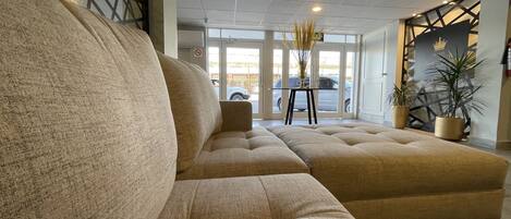 A modern hotel lobby with a large beige sofa, a small table with a vase, and a potted plant.