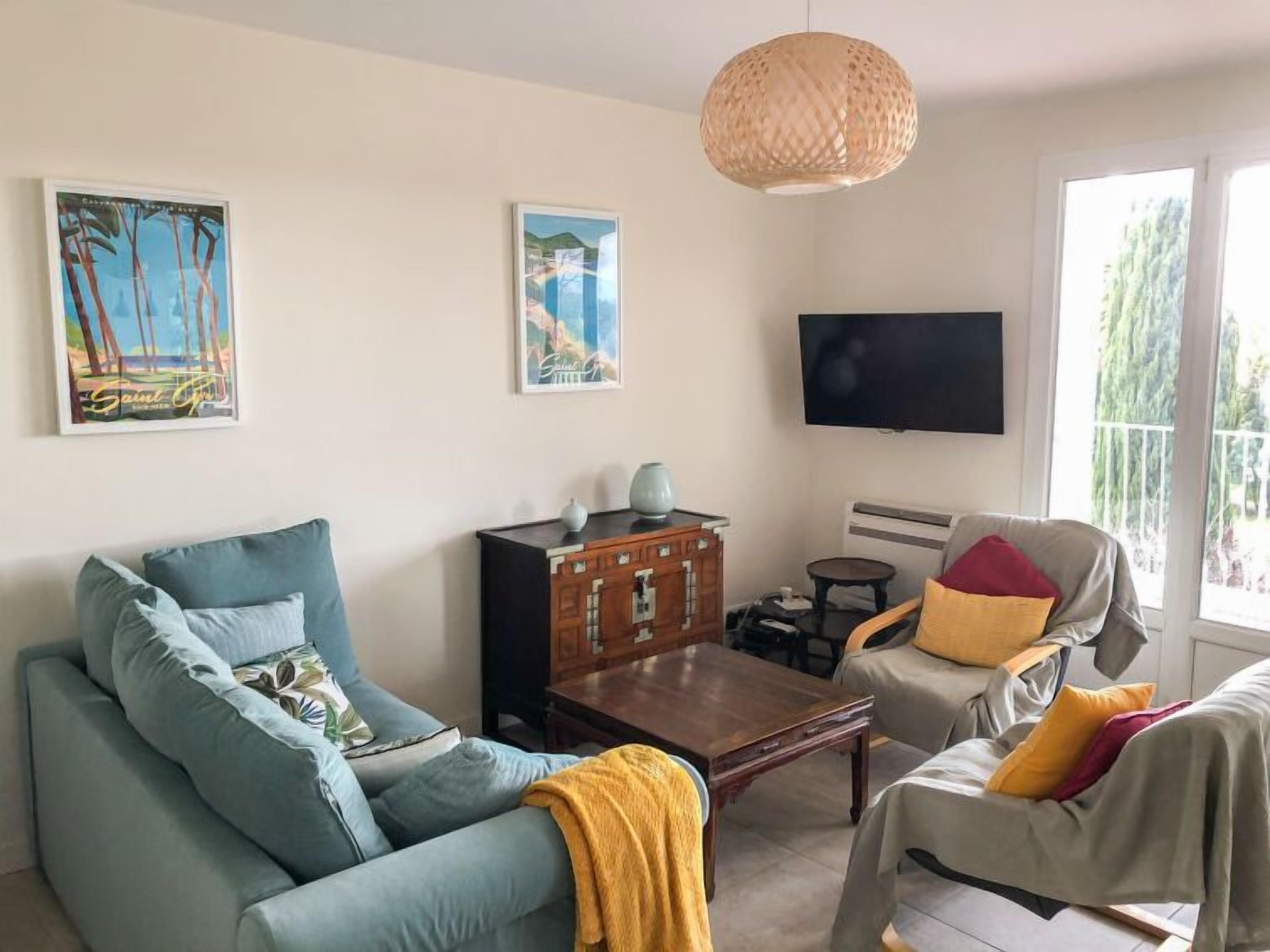Una sala de estar con sofá, sillón, mesa de centro y televisor montado en la pared.