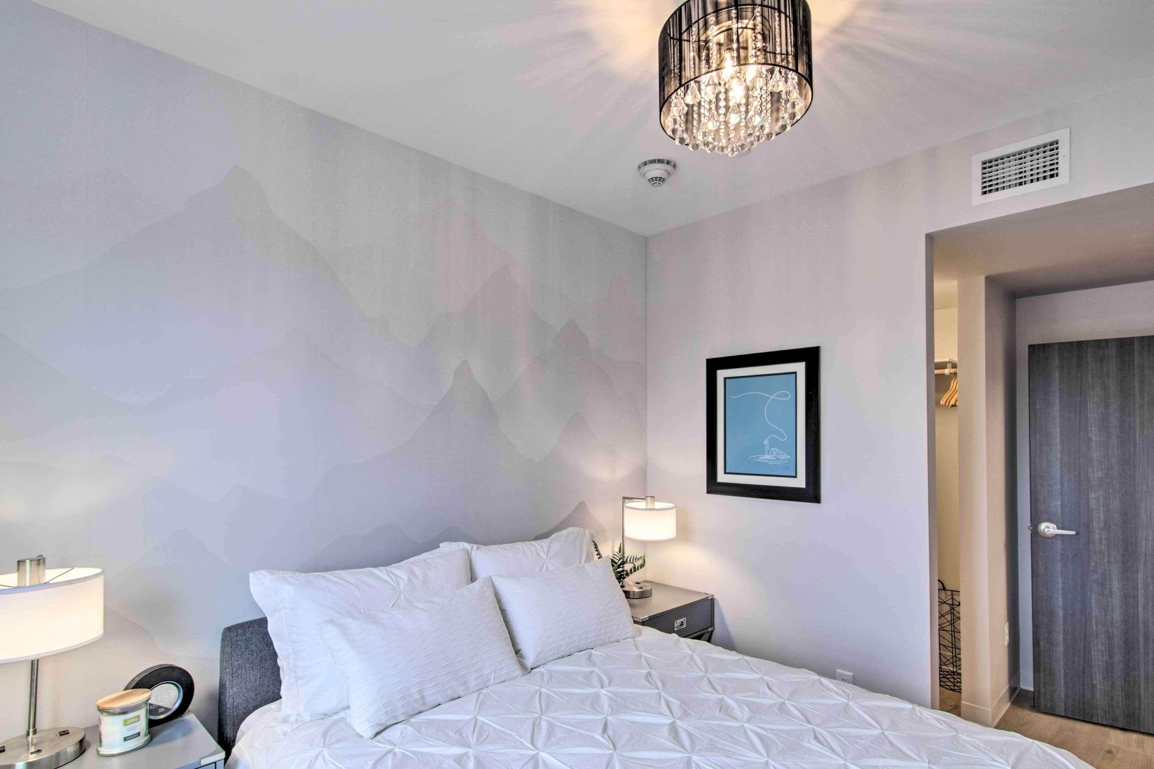 Une chambre d’hôtel avec un lit, une table de chevet, une lampe, un tableau encadré au mur et une porte.