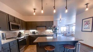A modern kitchen with dark cabinets, a large island with stools, a microwave, and a sink. - Luxury Ski-In/Out Condo – 305 Soaring Eagle, Stunning Sunrise Views & Hot Tubs! (Snowshoe)