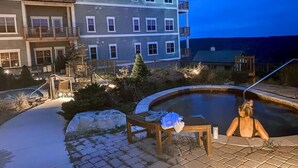 A swimming pool area with a wooden bench and a chair, surrounded by a stone pathway and a building with multiple balconies. - Luxury Ski-In/Out Condo – 305 Soaring Eagle, Stunning Sunrise Views & Hot Tubs! (Snowshoe)