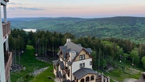 A multi-story house with a stone facade, multiple balconies, and a view of a forested valley. - Luxury Ski-In/Out Condo – 305 Soaring Eagle, Stunning Sunrise Views & Hot Tubs! (Snowshoe)
