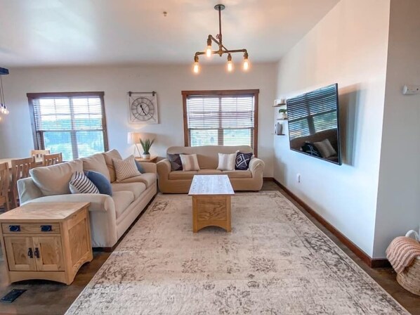 A spacious living room with a beige sofa set, a wooden coffee table, and a large window with blinds. - Luxury Ski-In/Out Condo – 305 Soaring Eagle, Stunning Sunrise Views & Hot Tubs! (Snowshoe)