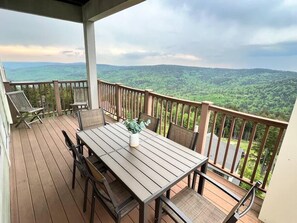 A wooden deck with a table and chairs, overlooking a lush green landscape. - Luxury Ski-In/Out Condo – 305 Soaring Eagle, Stunning Sunrise Views & Hot Tubs! (Snowshoe)