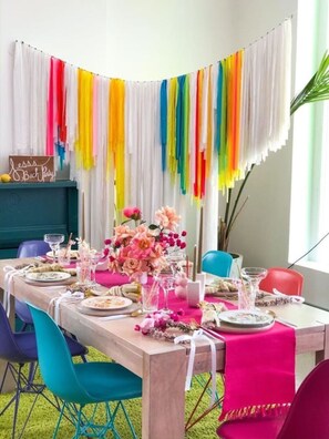 Un coin repas avec une table dressée pour une fête, des rideaux aux couleurs vives et une pancarte sur laquelle on peut lire : « Fête entre filles chez Jessie ».