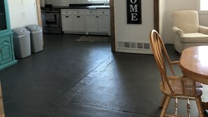 Ett rymligt vardagsrum med ett mörkt golv, ett träpanelat tak och en skylt med texten ”VÄLKOMMEN”. Ett matbord med stolar står i förgrunden.