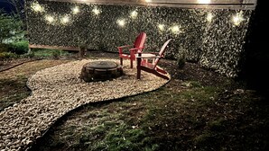 An outdoor seating area with a wooden bench and a fire pit, surrounded by a wooden pergola and string lights. - Cozy cottage condo with easy access to TIEC, Hendersonville, Asheville & Boone (Rutherfordton)