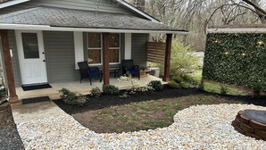 A house with a covered porch, outdoor seating, and a landscaped garden with pebbles and greenery. - Cozy cottage condo with easy access to TIEC, Hendersonville, Asheville & Boone (Rutherfordton)