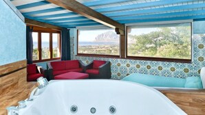 A room with a large bathtub, red and grey seating, and large windows offering a view of a mountainous landscape. - Le Palme by Interhome (Valderice)