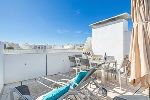 Een terras op het dak met een eettafel, stoelen en een tafellamp.