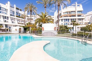 Una piscina con borde curvo, rodeada de palmeras y edificios modernos con balcones.